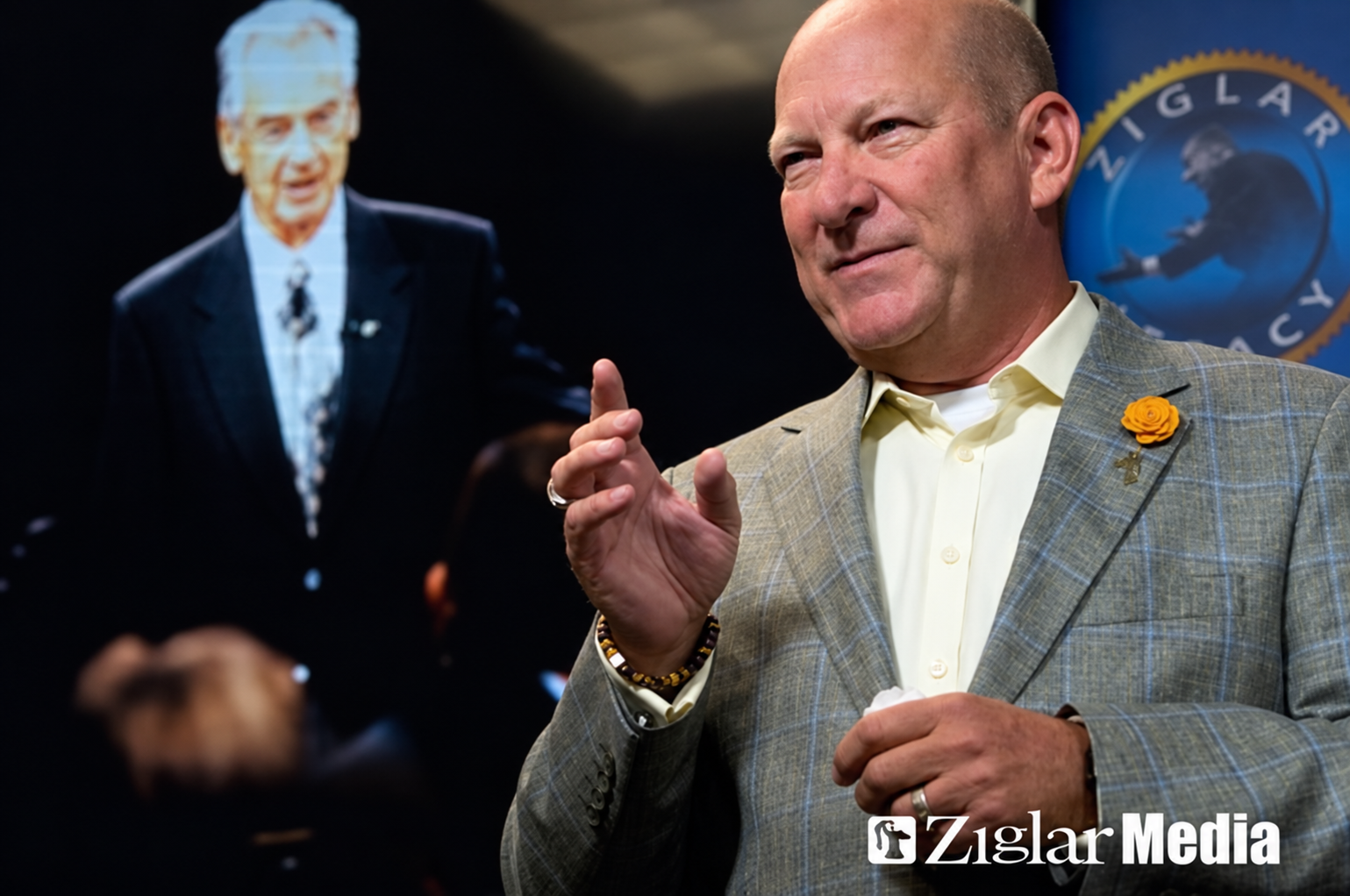 Jim Steinmark speaking at Ziglar with Zig Ziglar visible on the screen behind him.